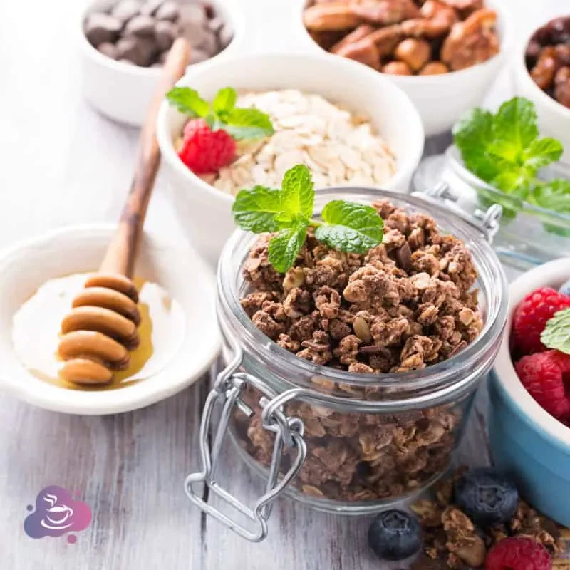 Gesunde Frühstücksschüssel mit Granola, Früchten, Nüssen und Honig auf rustikalem Holzbrett.