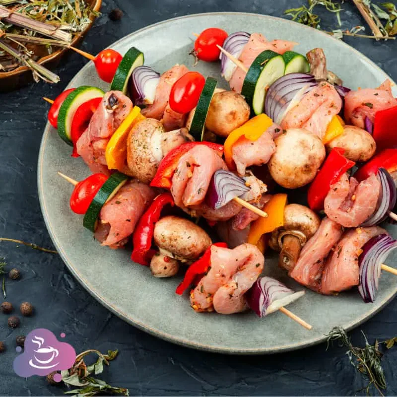 Bunte Grillspieße mit frischem Gemüse, mariniertem Fleisch und aromatischen Kräutern auf blauem Teller