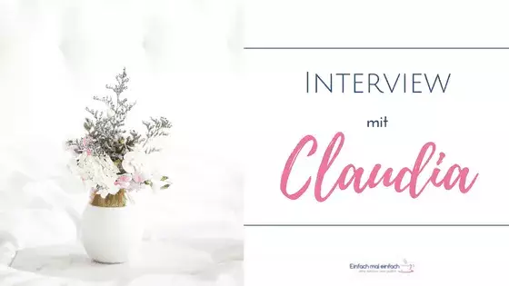Weiße Vase mit lila und weißen Blumen auf Marmortablett vor hellem Hintergrund. Text:"Interview mit Claudia"