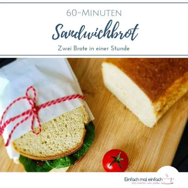 Weißes Kastenbrot auf Holzbret mit Sandwich in Butterbrottüte und rotem Garn zugebunden. Tomaten, Salat und dunkle Soße auf dem belegten Brot.