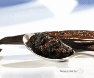Vanillepaste auf Löffel mit Vanilleschoten im Hintergrund.