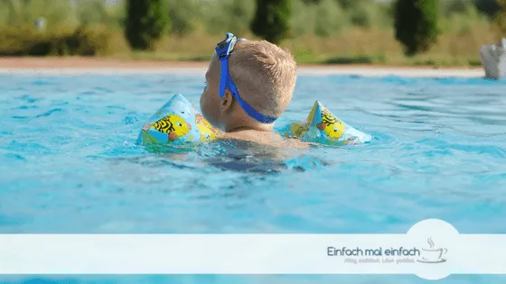 Kleinkind im Pool mit Schwimmflügeln und Sonnenbrille