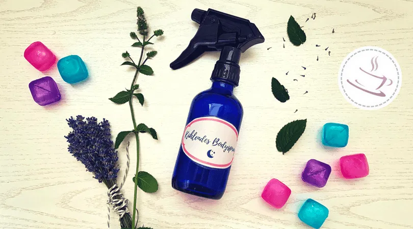 Blaue Sprühflasche auf hellem Untergrund mit Pfefferminze, Lavendel und bunten Eiswürfeln.