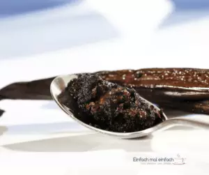 Vanillepaste auf Löffel mit Vanilleschoten im Hintergrund.