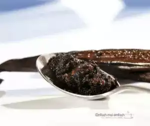 Vanillepaste auf Löffel mit Vanilleschoten im Hintergrund.