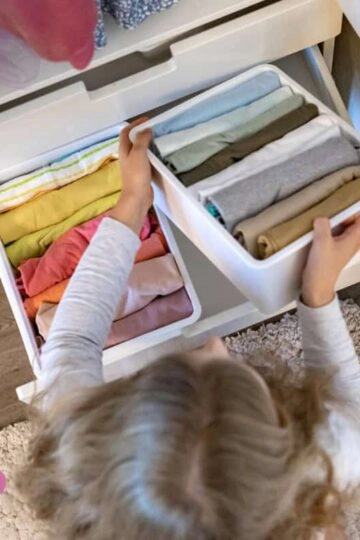 Kind, ordentliches Kinderzimmer beim Aufräumen und Kleidung sortieren für mehr Unabhängigkeit.