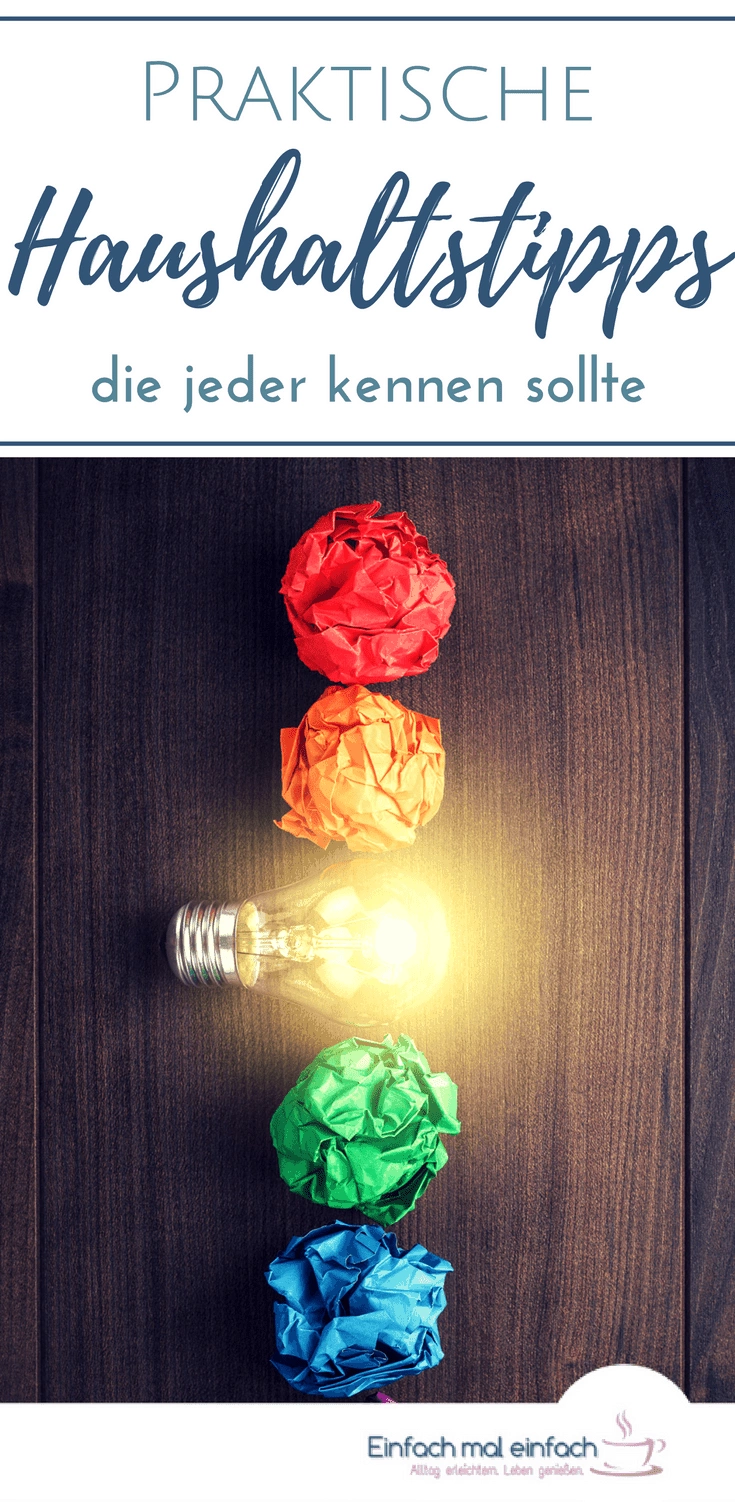Bunte Bälle aus zerknülltem Papier in Regenbogenfarben mit leuchtender Glühbirne in einer Reihe auf dunklem Holzuntergrund. Text: