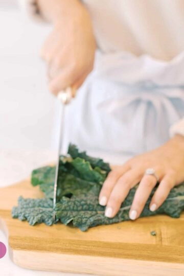Person schneidet frisches Grünkohl in gemütlicher, moderner Küche beim Kochen.
