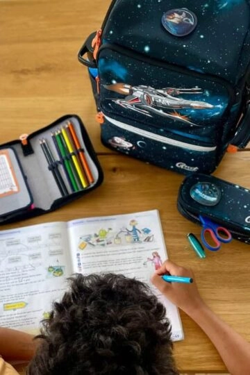 Kindergarten kind lernt kreativ mit buntem Schulzubehör und Abenteuerrucksack.