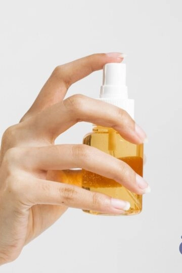 Hände halten ein elegantes Pumpspray mit goldenem Öl für Hautpflege oder Beauty.